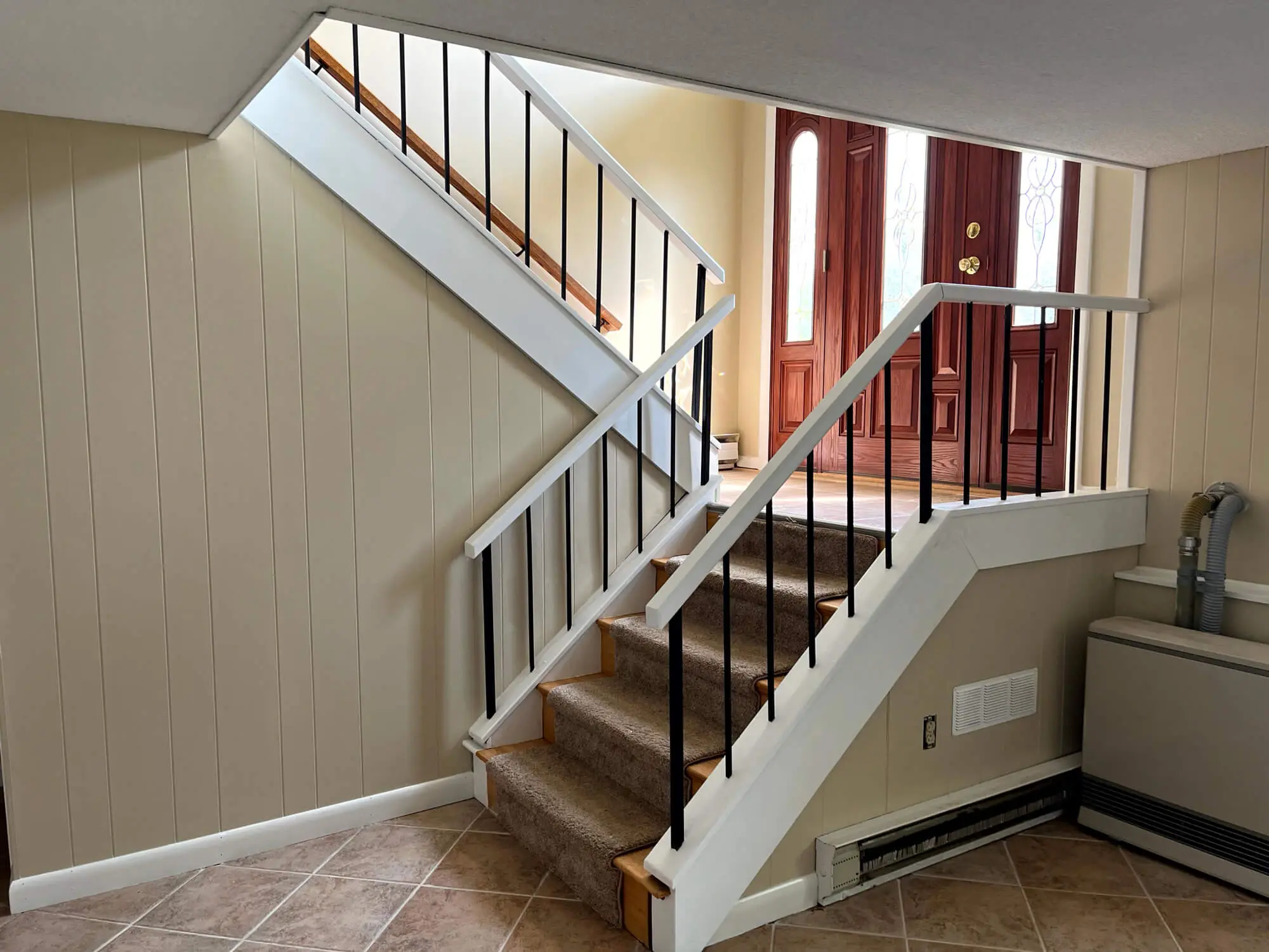 Professionally painted stairwell and entryway with smooth neutral walls, crisp white railings, and detailed trim work completed by Zellers Painting & Contracting.