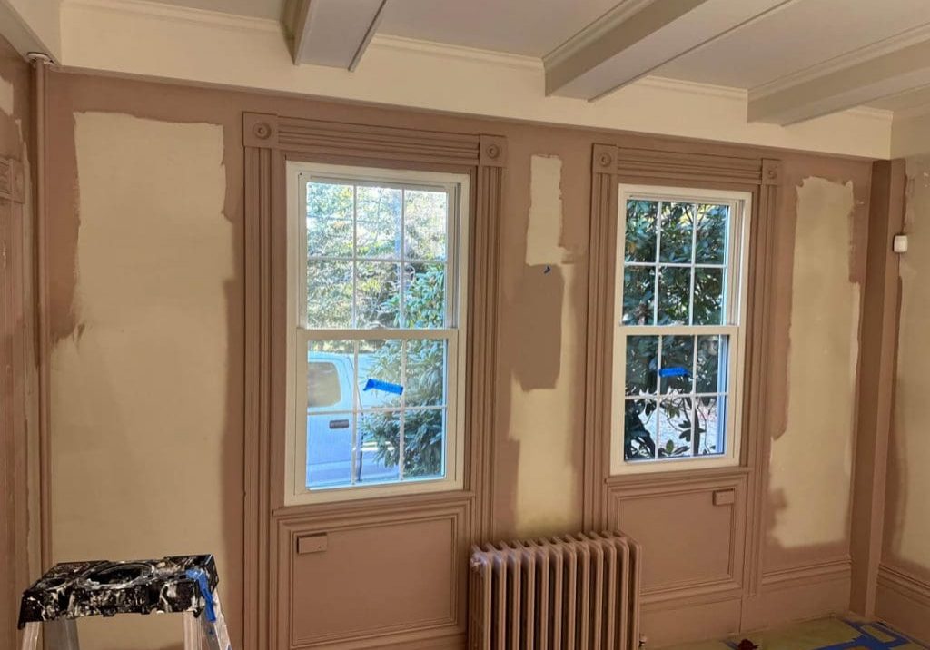 A room featuring ornate window trim and walls being meticulously prepped and painted in a dusty rose finish by Zellers Painting.